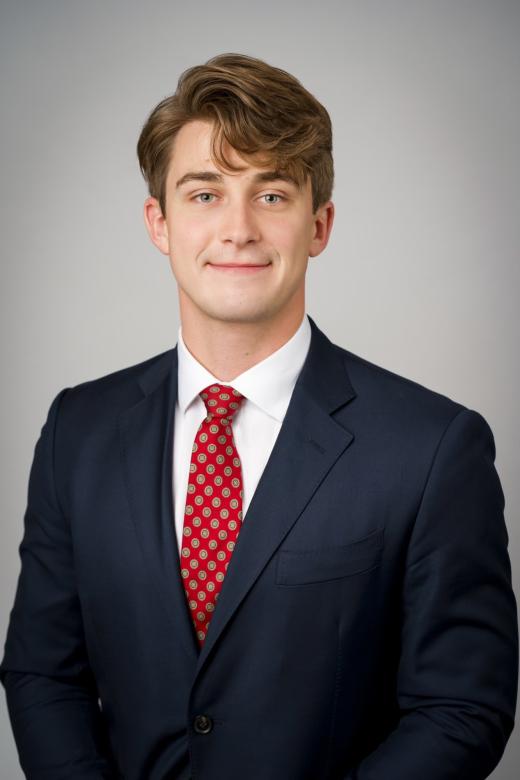 Headshot of Ari Anderson wearing a blue suit with a red tie